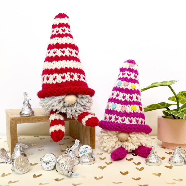 Two knitted Lots of Love Gnomes sit surrounded by Hershey's kisses.